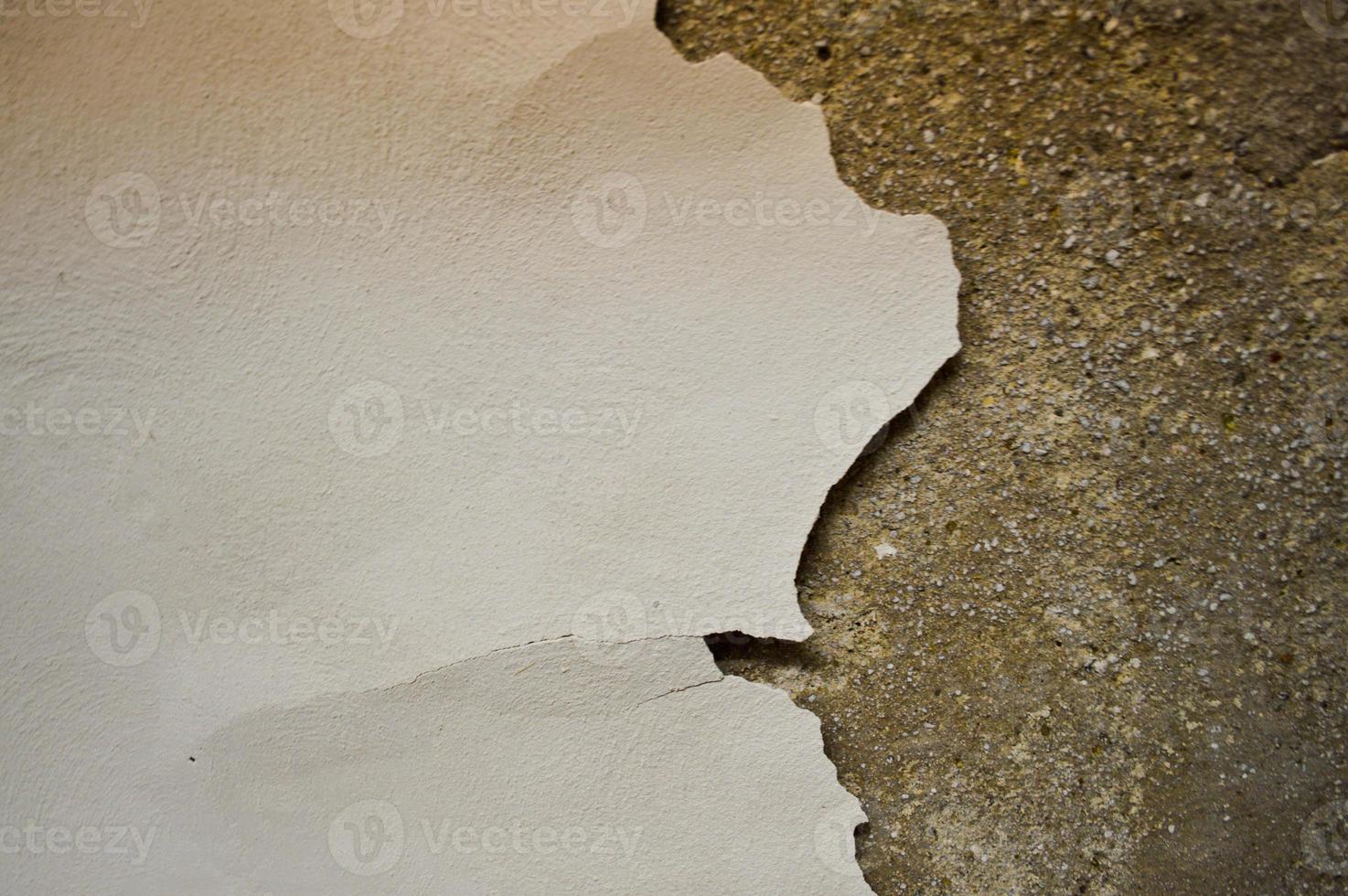 The texture of the stone concrete old shabby wall with cracks and chips with whitewashing and exfoliated plaster, putty. The background photo