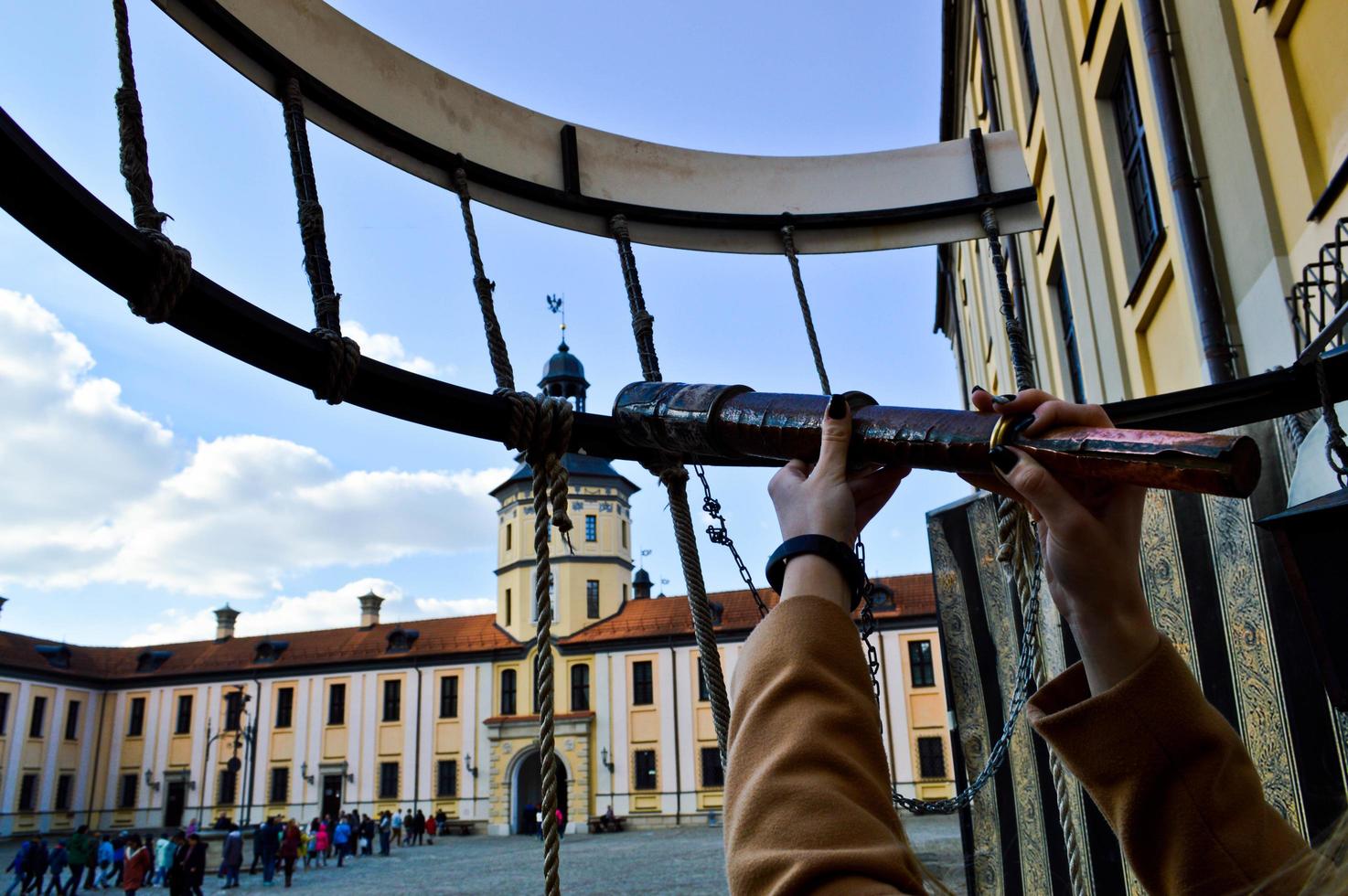 The girl, the woman looks in an old ancient telescope on the European medieval tourist building, the castle, the palace with a spire and a tower on the square photo