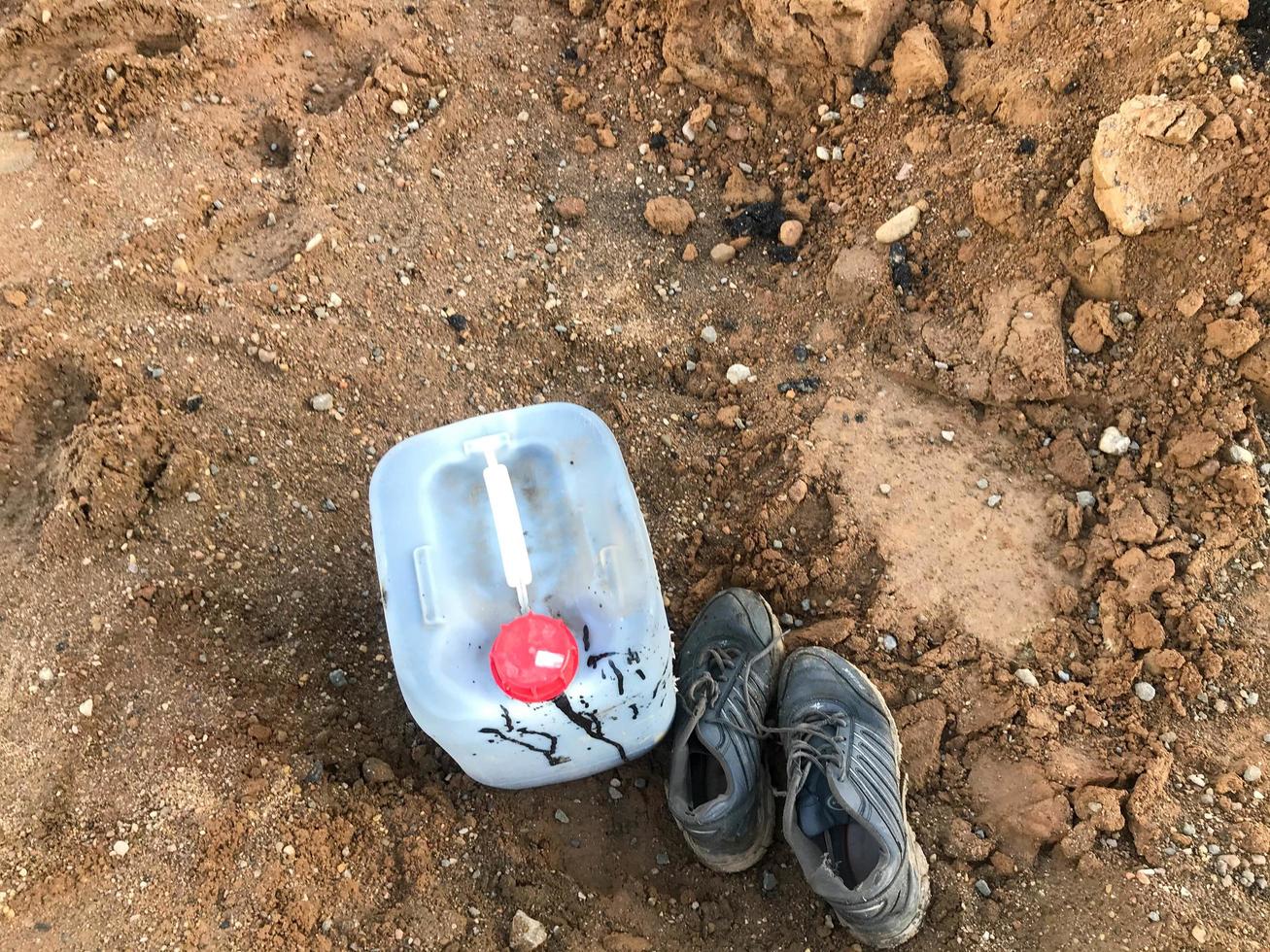 a white construction canister with a red lid is on the ground. the canister is smeared with fuel oil. the builders' boots are nearby. construction site, container for transferring various liquids photo