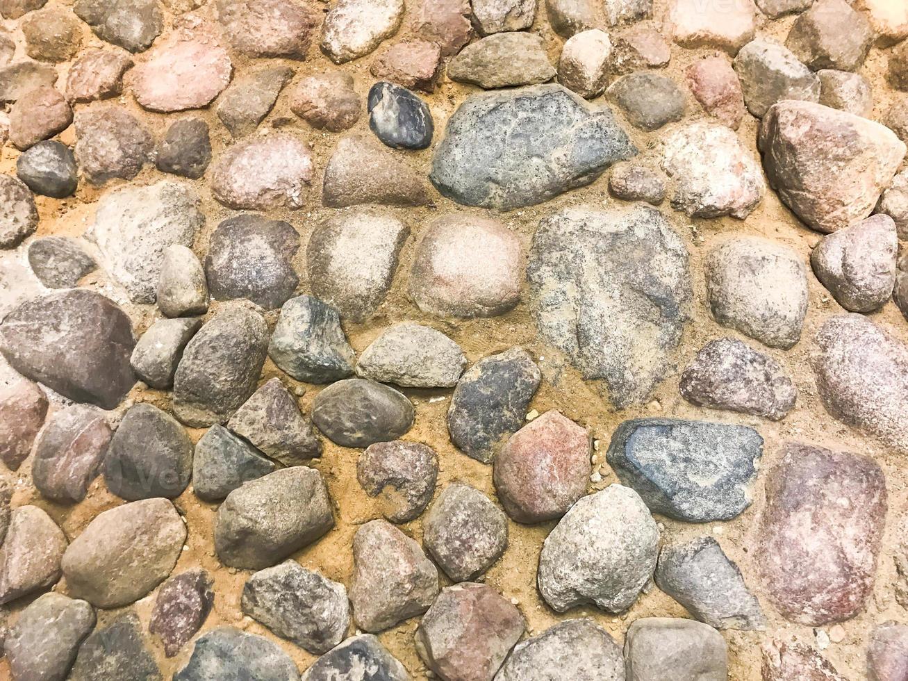 The texture of the stone road, pavement, walls of large gray old medieval round strong stones, cobblestones. The background photo