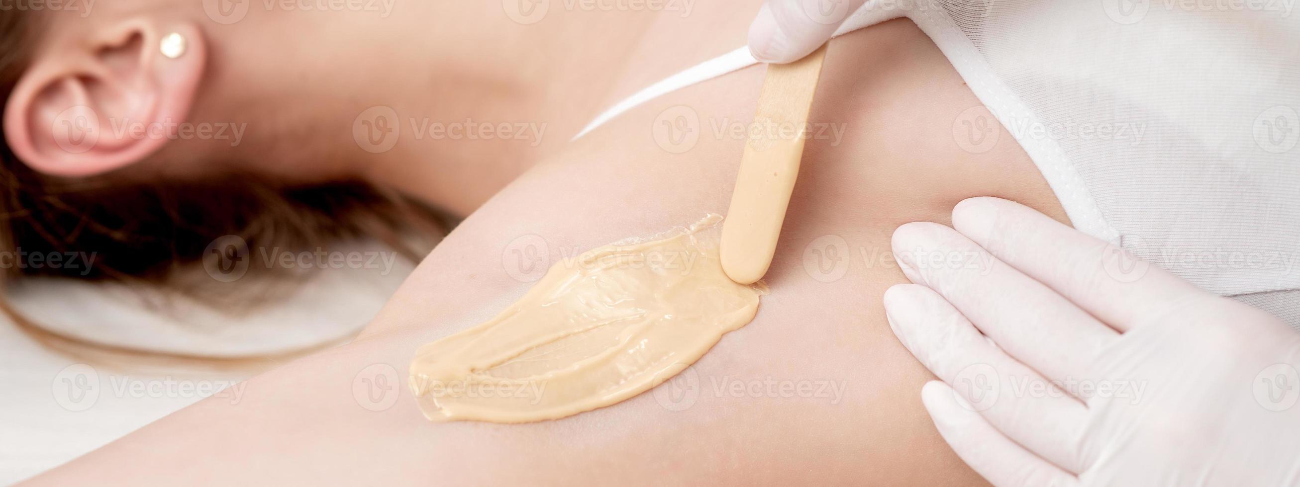 Cosmetologist applying wax paste on armpit photo