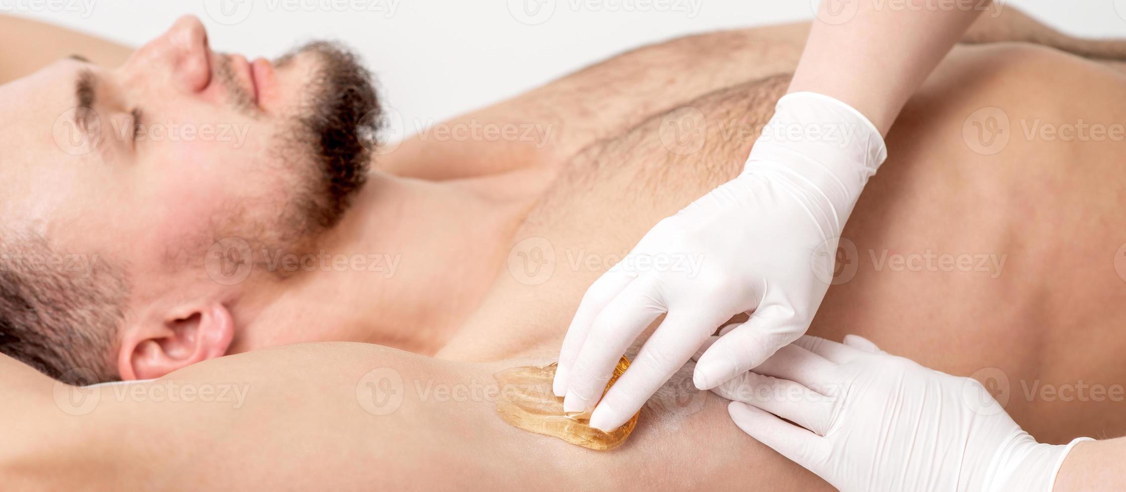 Cosmetologist applying wax paste on male armpit photo