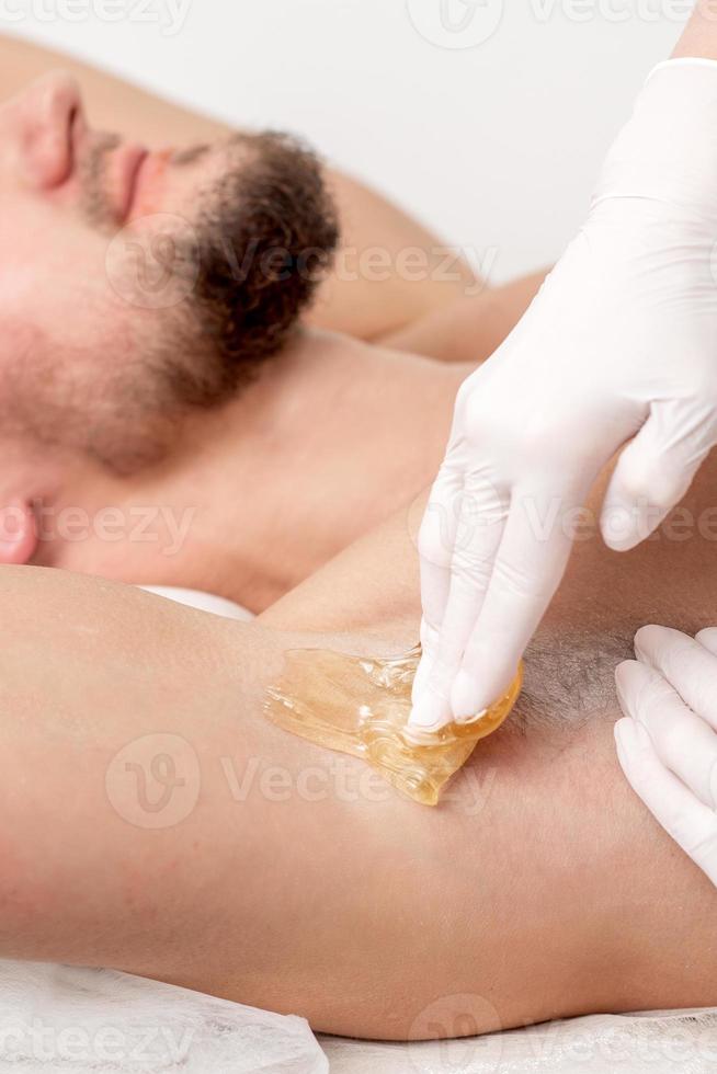 Cosmetologist applying wax paste on male armpit photo
