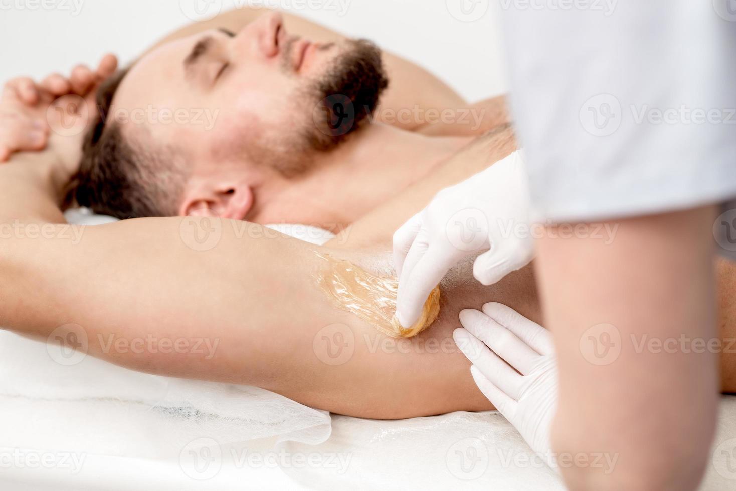 Cosmetologist applying wax paste on male armpit photo