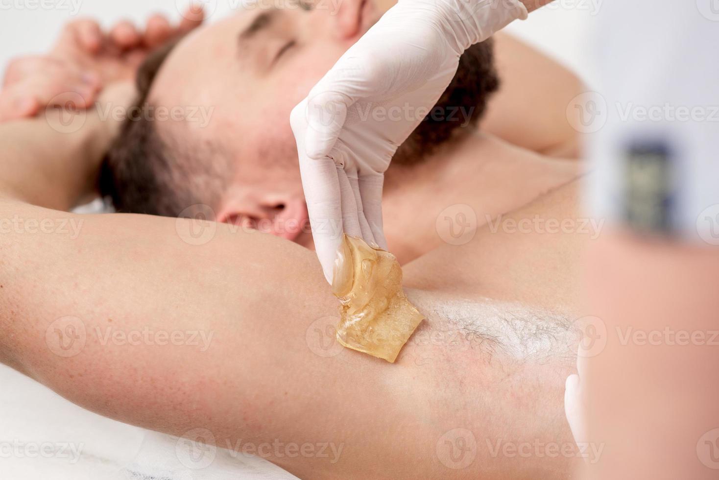 Cosmetologist applying wax paste on male armpit photo