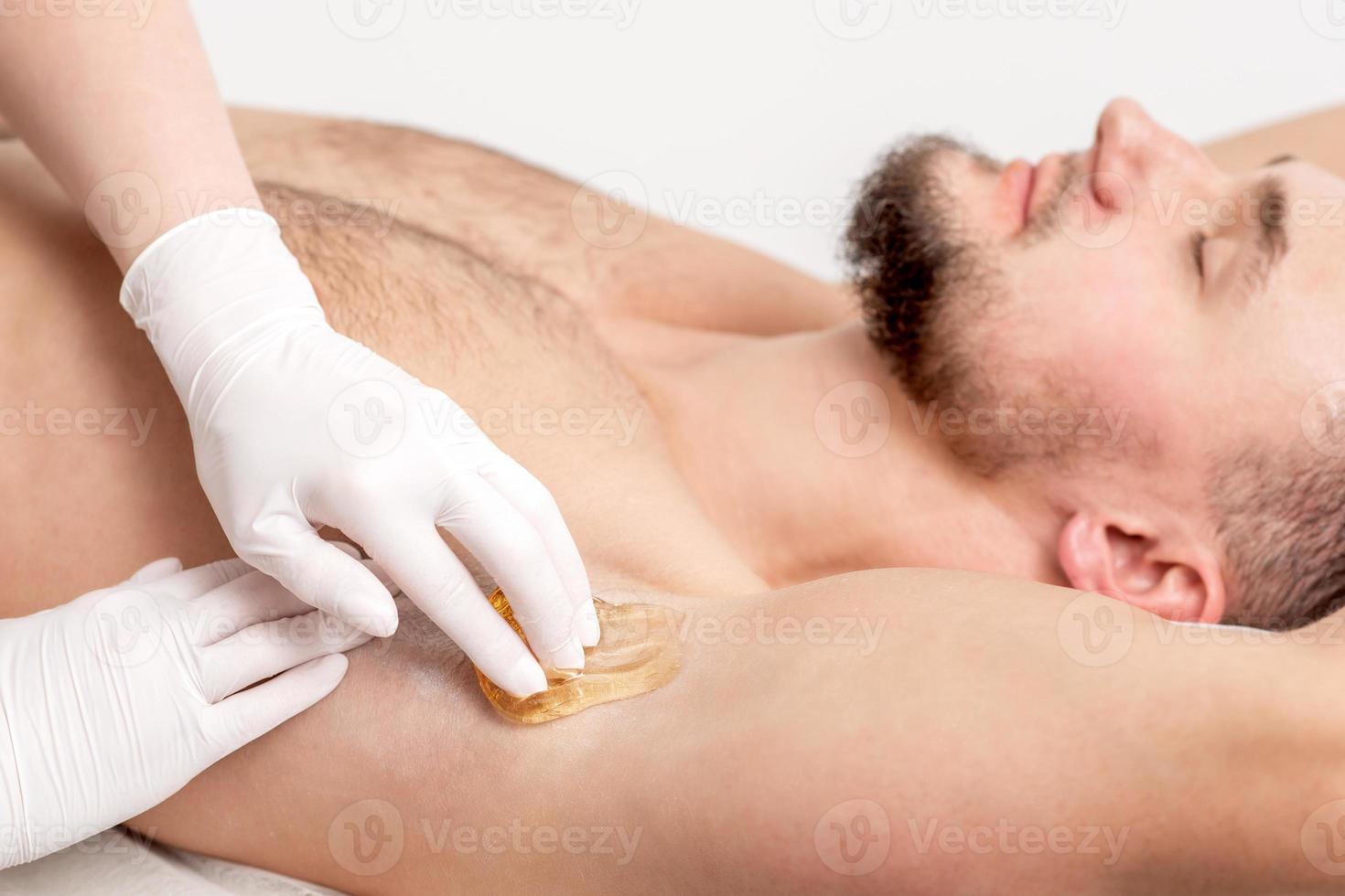 Cosmetologist applying wax paste on male armpit photo