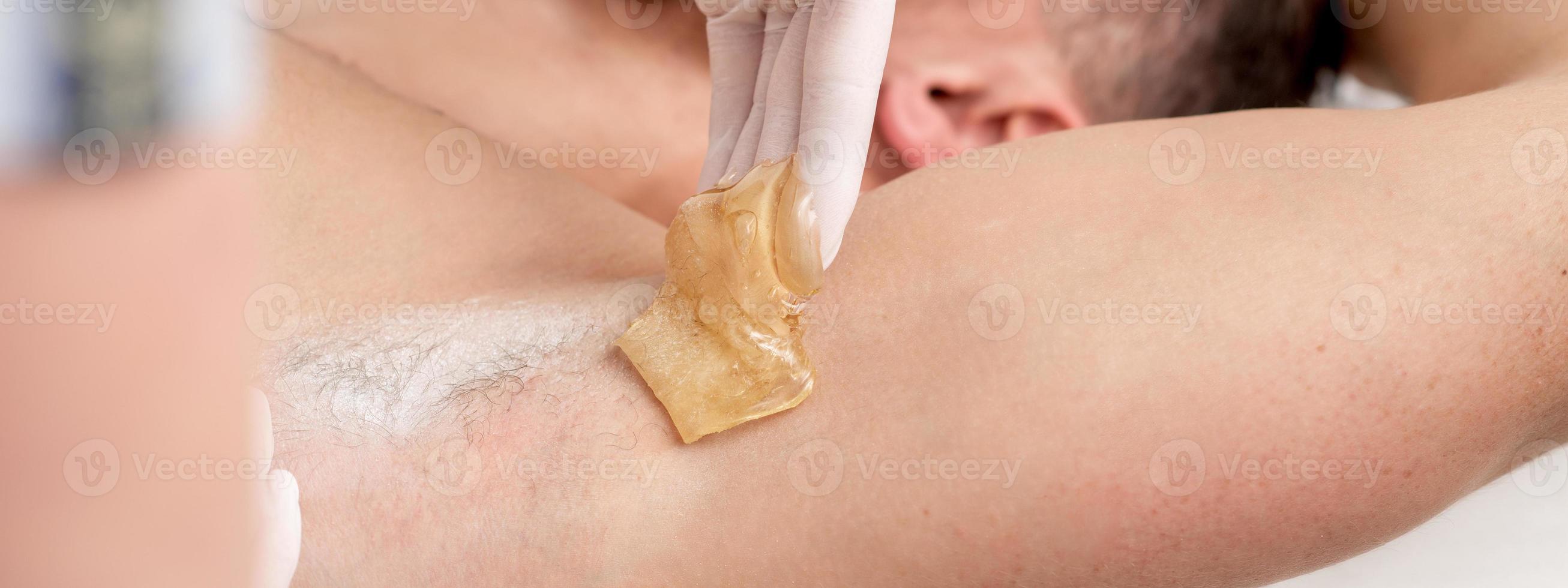 Cosmetologist applying wax paste on male armpit photo