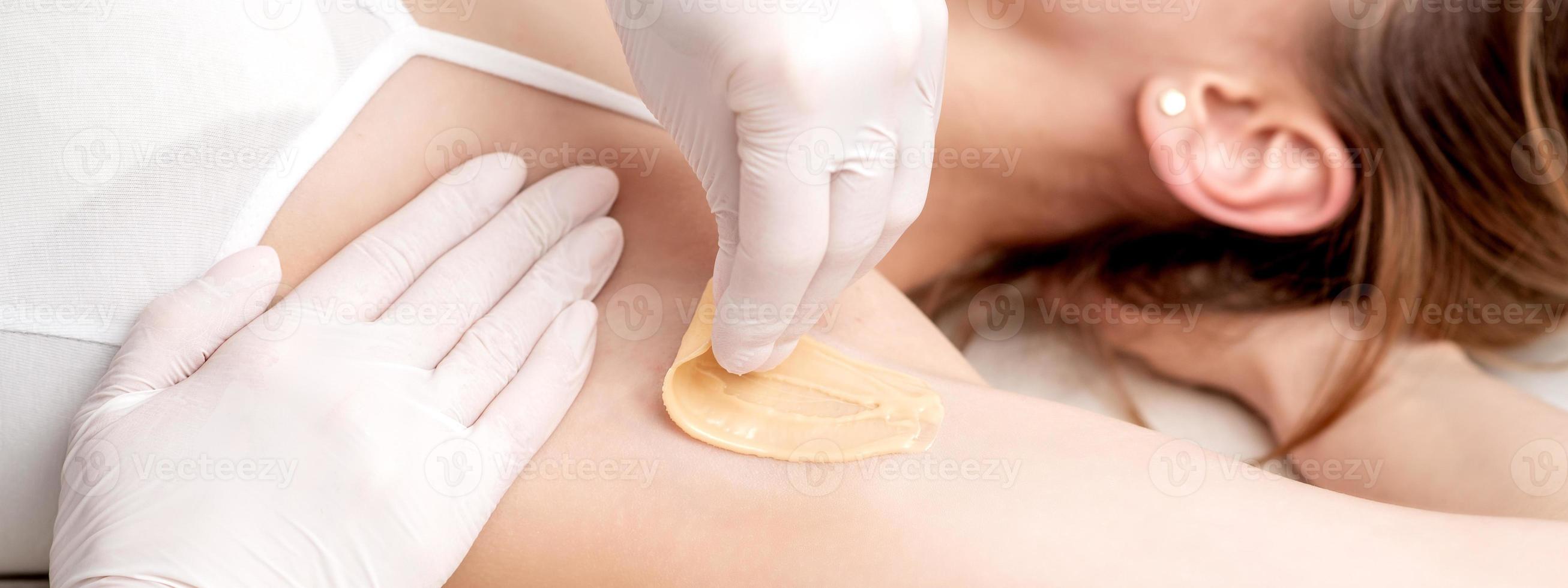 Cosmetologist applying wax paste on armpit photo