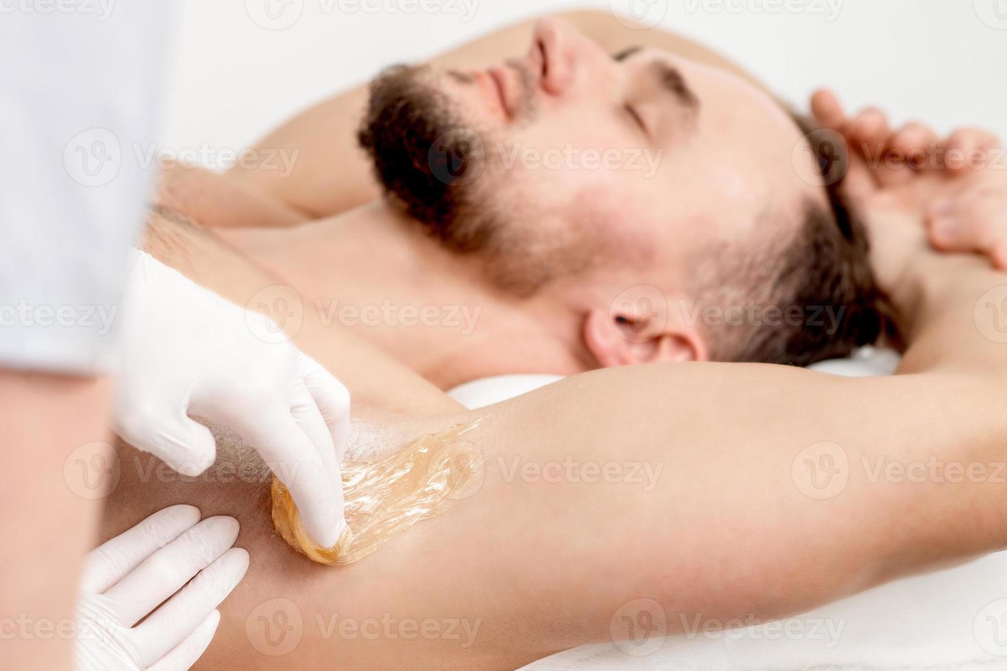 Cosmetologist applying wax paste on male armpit photo