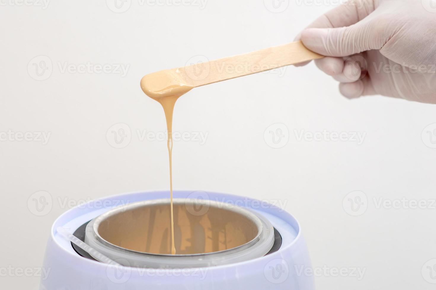 Wax heater with hot wax on wooden spatula photo