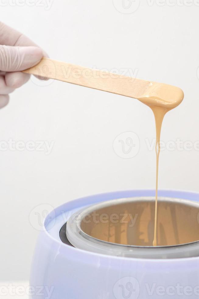 Wax heater with hot wax on wooden spatula photo