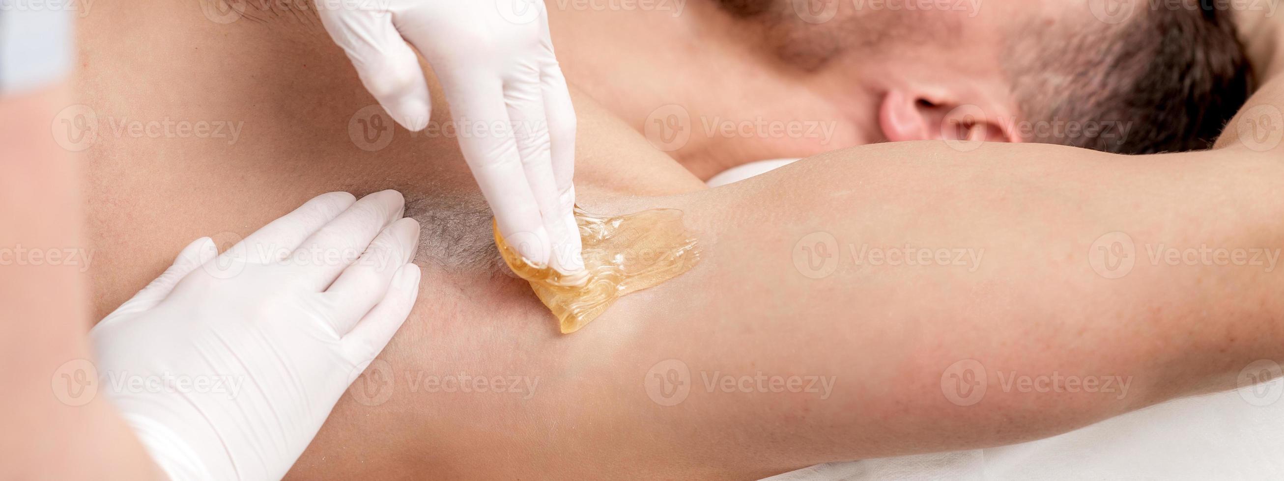 Cosmetologist applying wax paste on male armpit photo