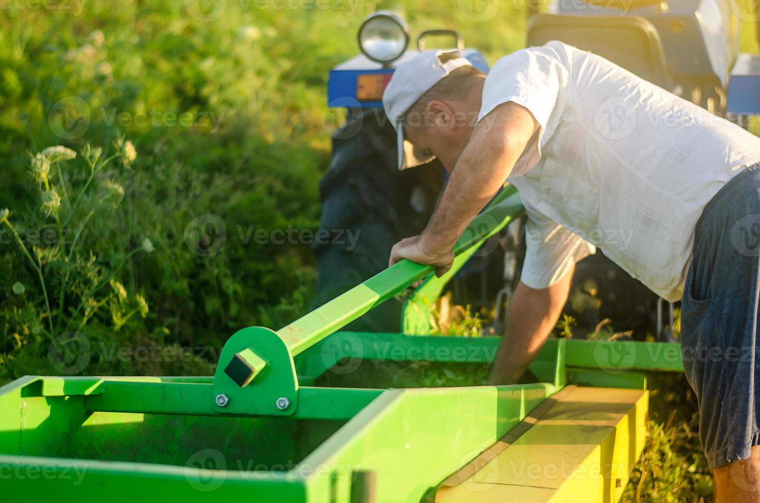 A farmer examines the process of digging up potato tubers with a digger machine. Extract root vegetables to surface. Farming agriculture and farmland. Harvesting potatoes in autumn. photo