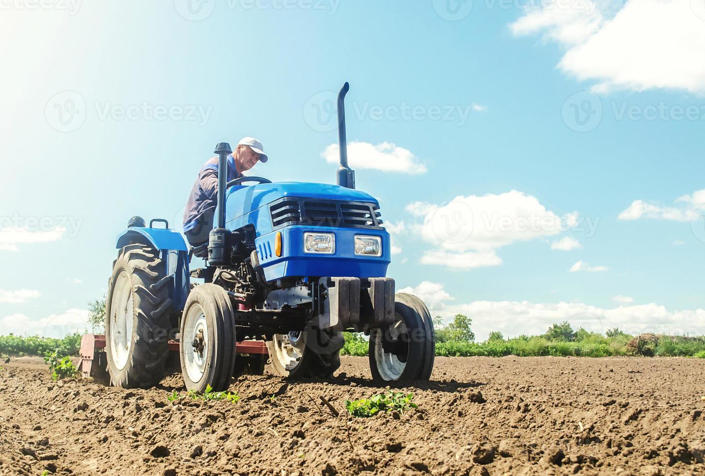 The farmer works on a tractor. Loosening the surface, cultivating the land for further planting. Grinding and loosening soil, removing plants roots from last harvest. Cultivation technology equipment. photo