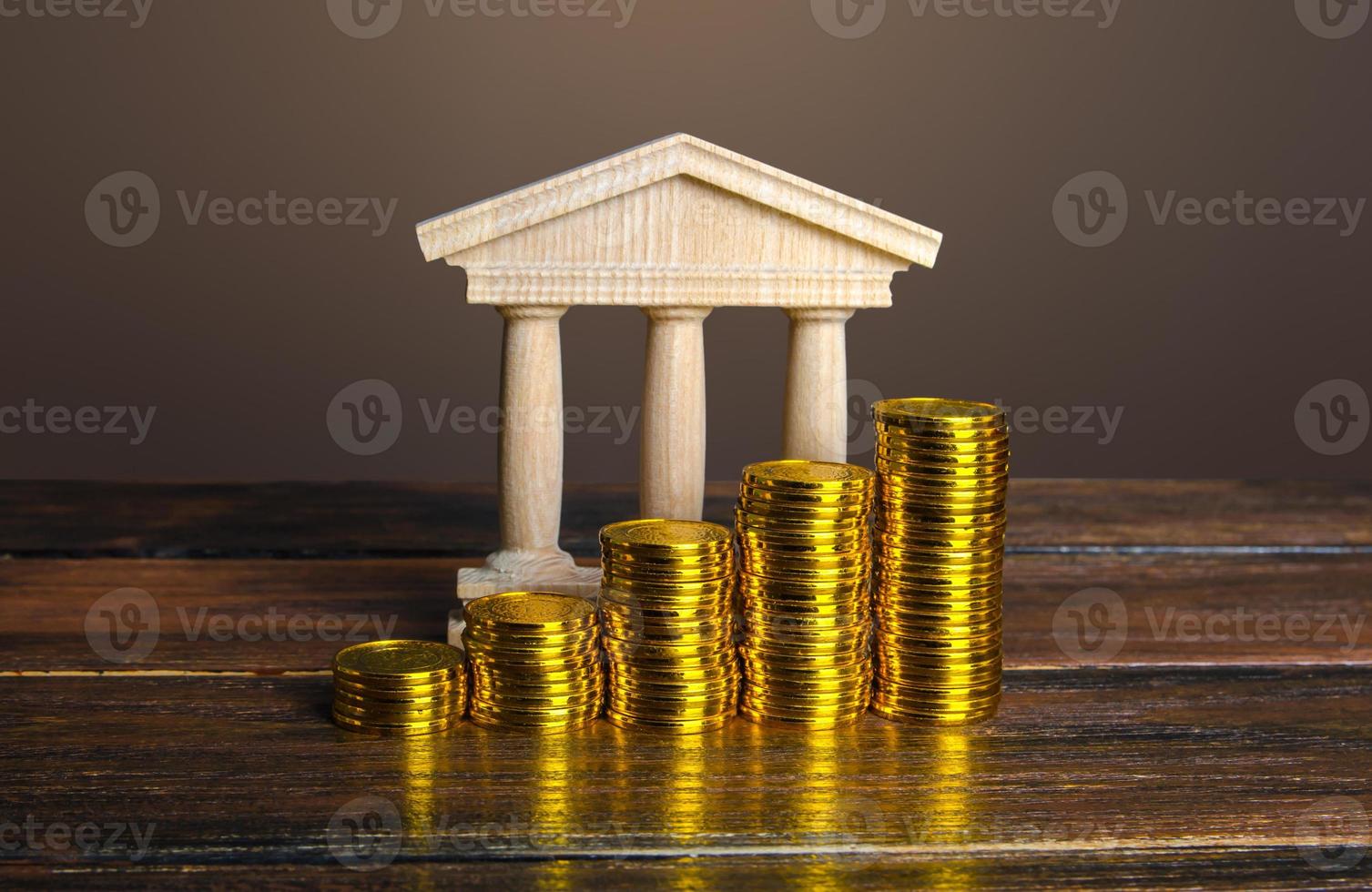 Bank building and increasing stacks of coins. Profitability of deposits and favorable rates for depositors, loyalty programs. Income growth. Increasing taxes collected. Budgeting. Monetary policy. photo