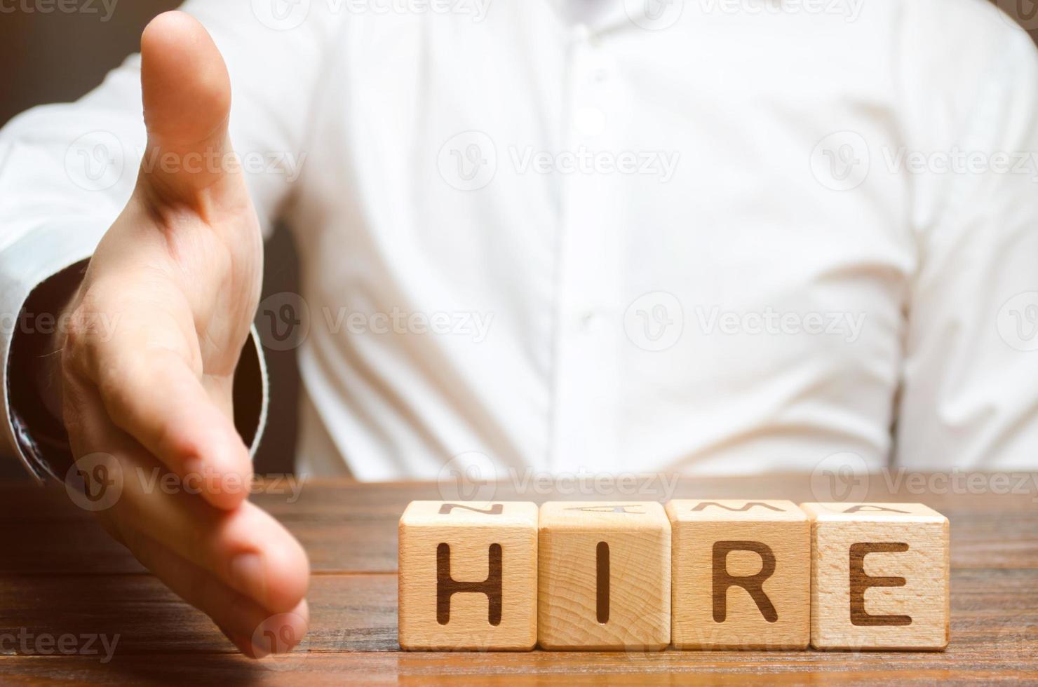 A businessman holds out his hand to shake hands and agree to hire on the background of the word hire. Recruitment concept. Search for employees and professionals on favorable terms. photo