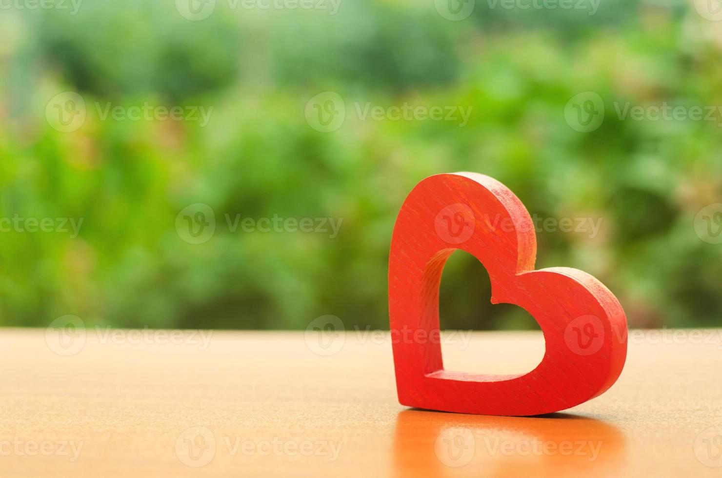 un corazón de madera rojo sobre fondo de naturaleza. el secreto de las relaciones y las reglas de una familia fuerte. fuerte historia de amor. secretos, rumores y chismes. concepto de salud íntima femenina. la salud del corazón foto