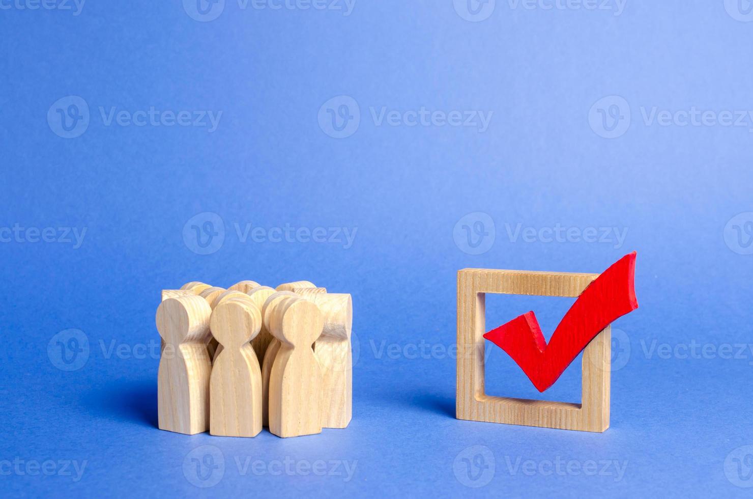 multitud de personas mirando una marca de verificación de madera roja para votar en las elecciones sobre un fondo azul. elecciones presidenciales o parlamentarias, un referéndum. encuesta de la población, estadística tarea completada foto