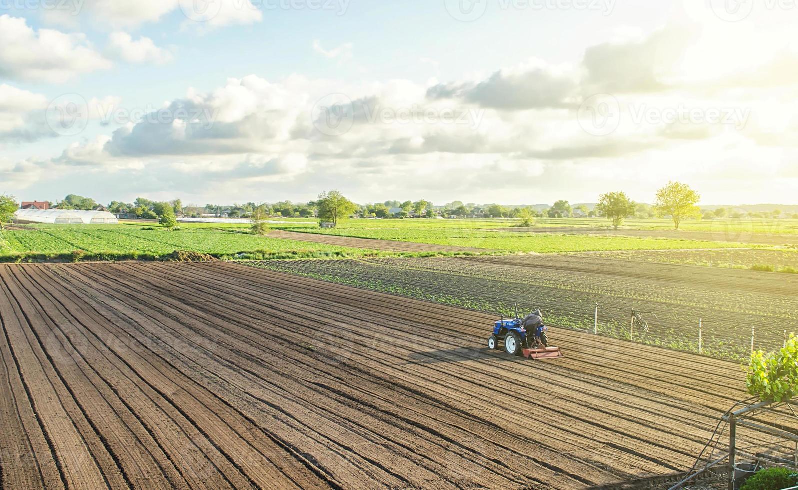 A tractor rides on a farm field. Farmer on a tractor with milling machine loosens, grinds and mixes soil. Farming and agriculture. Loosening the surface, cultivating the land for further planting. photo