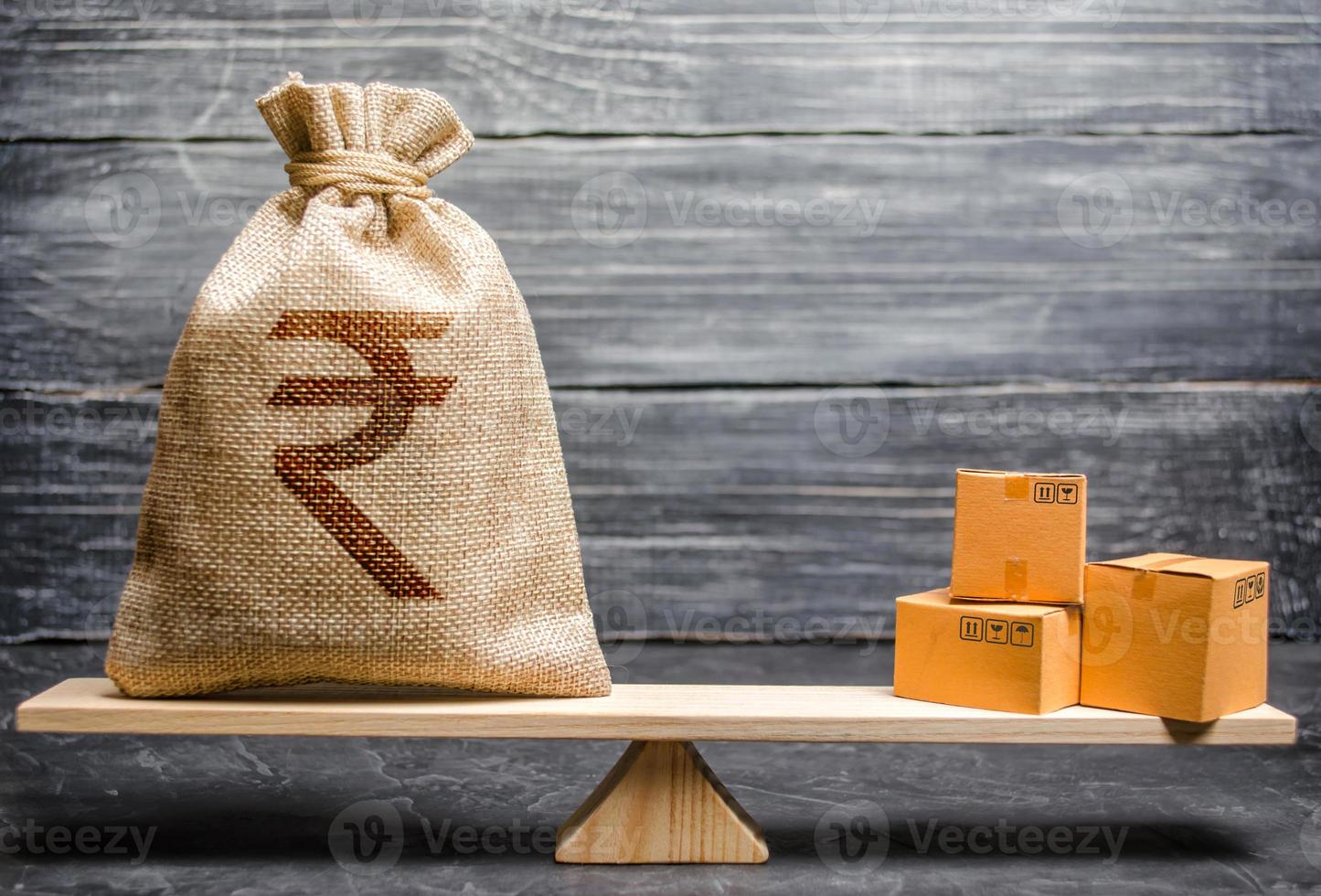 Indian rupee INR symbol money bag and a bunch of boxes on scales. Trade exchange balance. Import and export, economic processes. Profit from manufactured goods. Manufacturing, retail distribution photo