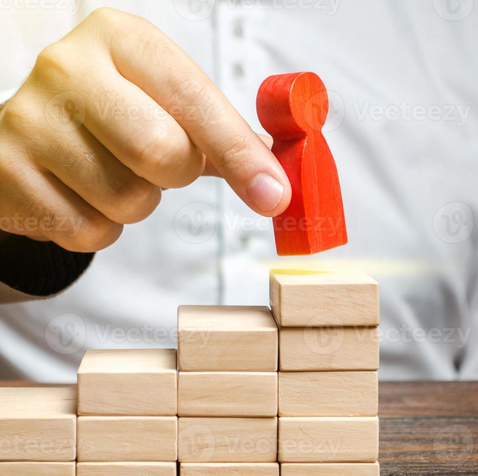 A man puts a red human figure on top of the stairs. Career growth, improvement of skills. Promotion at work of employees to leading post. The concept of success. Training. Education, business photo