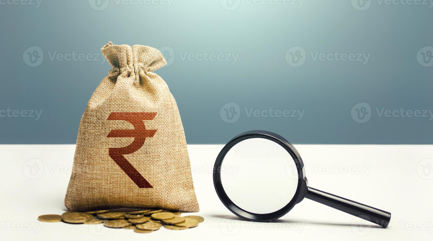 bolsa de dinero de la rupia india y lupa. auditoría financiera y seguimiento de capitales y transacciones sospechosas. búsqueda de beneficiarios comerciales. control de presupuesto captación de inversiones financiación. foto