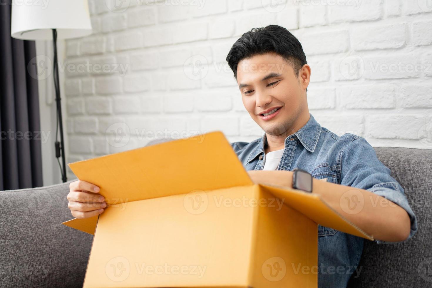 Young Asian man unpacking the parcel paper box. Happy man unpacking online Internet parcel at home, delivery service concept. photo