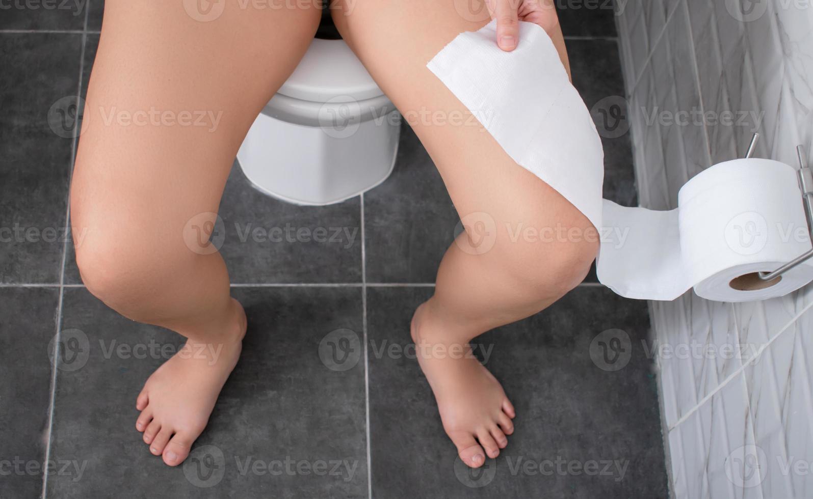 Asian person is sitting on a toilet bowl and pulling tissue in the toilet. photo