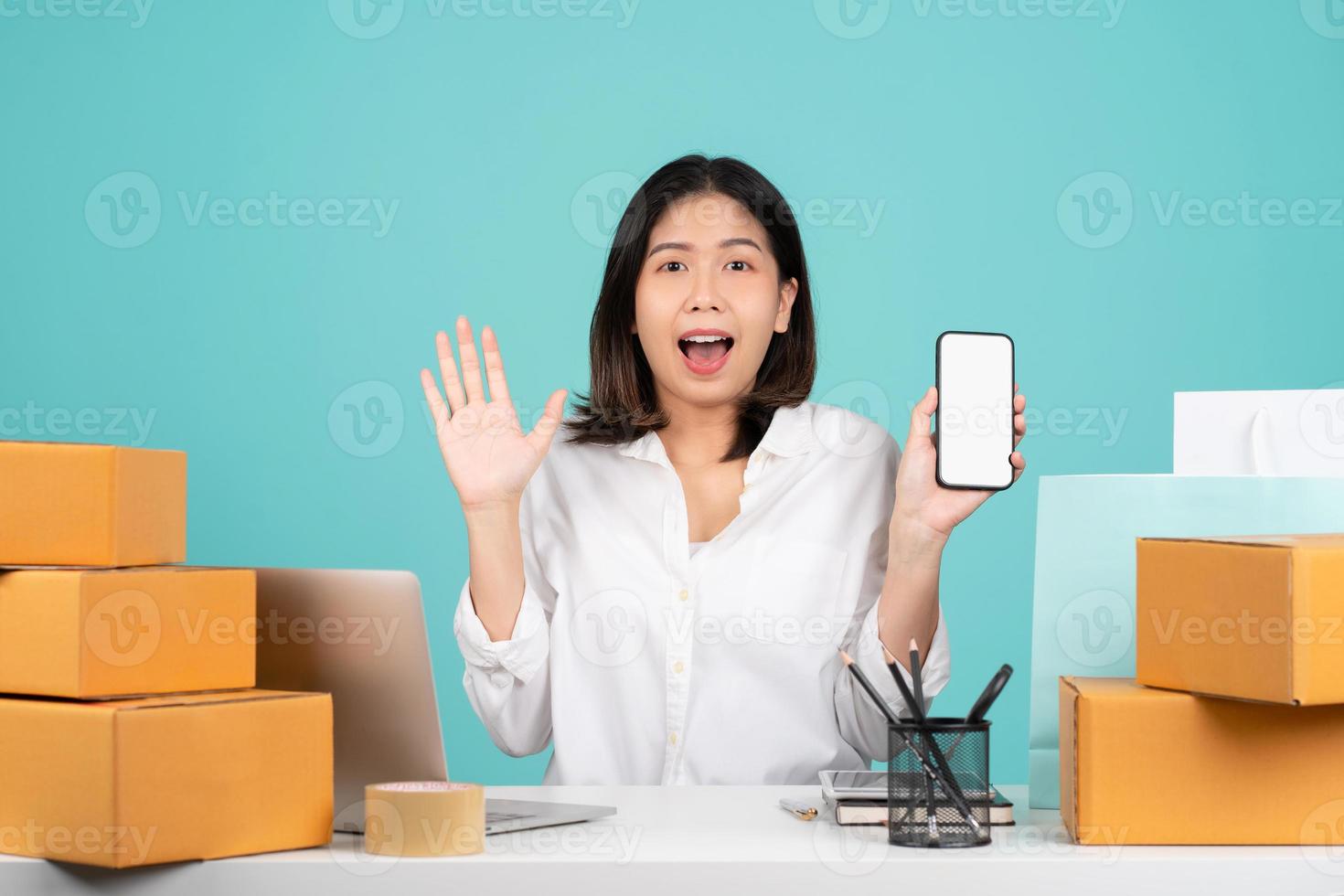 Asian businesswoman in a casual shirt sits at desk with a brown cardboard box. She holding a smartphone, the screen was blank and shocked. Isolated on a green background. photo