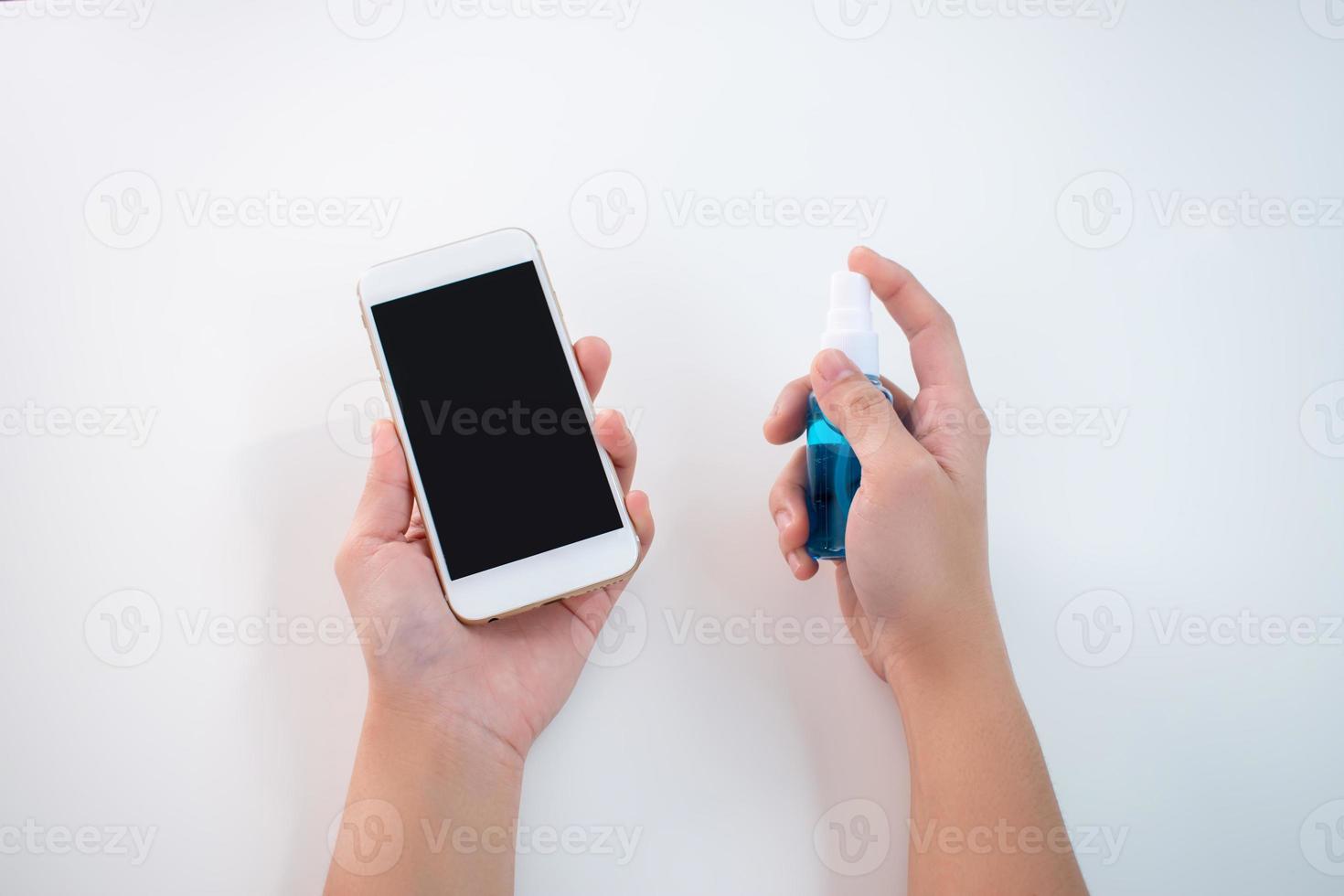 Asian woman uses an alcohol spray to clean her smartphone on a white background. photo