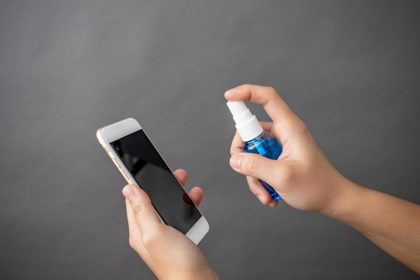 Close up of the hand with a spray of alcohol on the smartphone to clean. photo