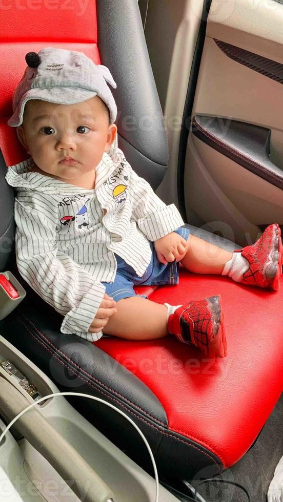A child sits in a red black car looking at the driver's face photo