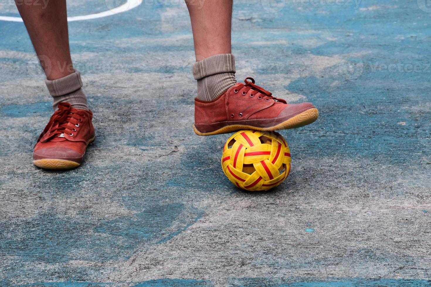 Young southeast asian male sepak takraw player using his right ankle to hold ball up on the serving center area of the court, outdoor sepak takraw playing after school, soft and selective focus. photo