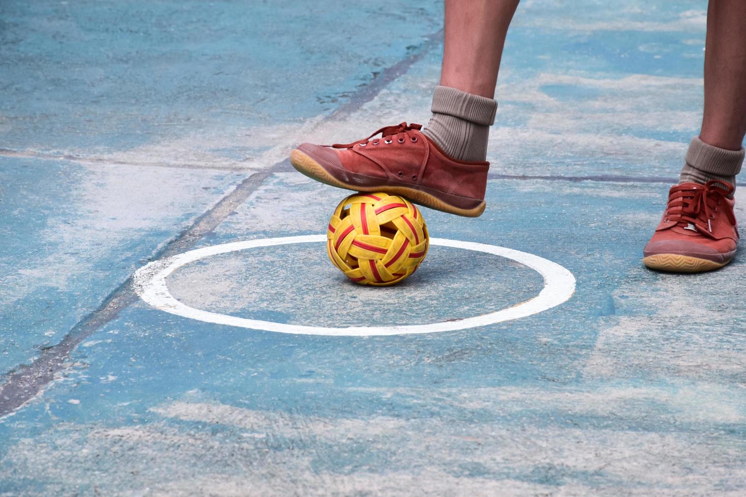 joven jugador de sepak takraw masculino del sudeste asiático usando su tobillo derecho para sostener la pelota en el área central de servicio de la cancha, sepak takraw al aire libre jugando después de la escuela, enfoque suave y selectivo. foto