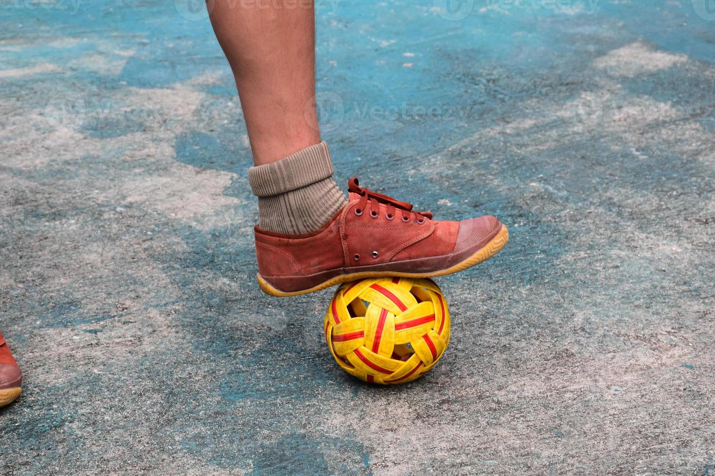 Young southeast asian male sepak takraw player using his right ankle to hold ball up on the serving center area of the court, outdoor sepak takraw playing after school, soft and selective focus. photo