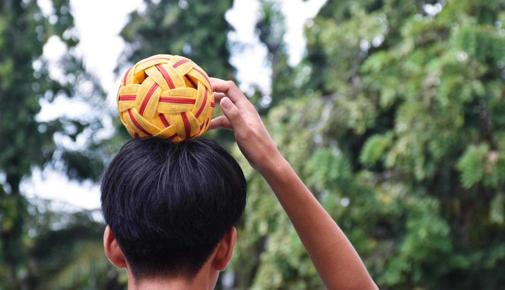 joven jugador de sepak takraw masculino del sudeste asiático usando su mano derecha para sostener la pelota en su cabeza, sepak takraw al aire libre jugando después de la escuela, enfoque suave y selectivo en la pelota. foto