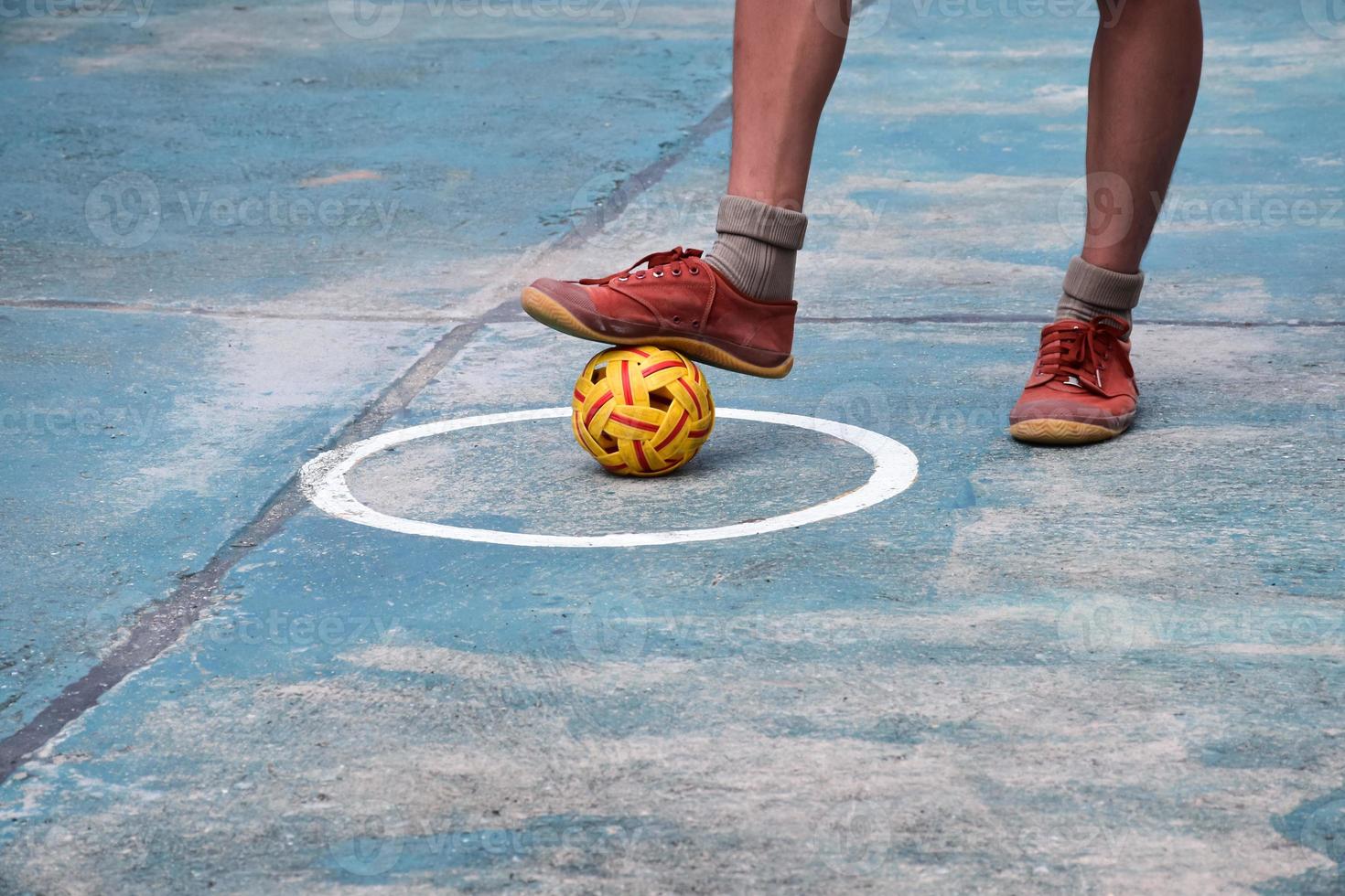 Young southeast asian male sepak takraw player using his right ankle to hold ball up on the serving center area of the court, outdoor sepak takraw playing after school, soft and selective focus. photo