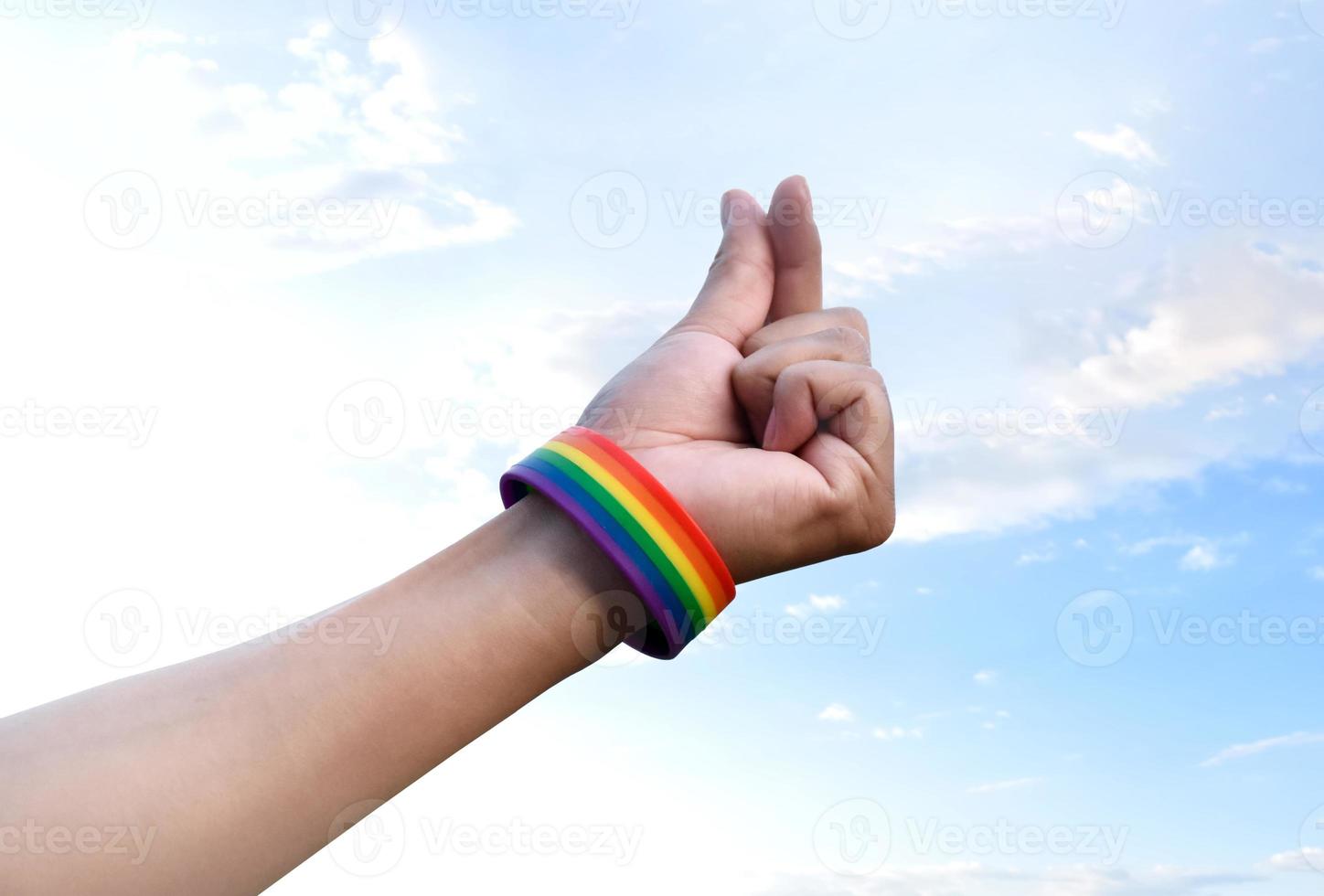 Hand of human which has rainbow wristband and doing mini heart or love sign by fingers, concept for presenting love to LGBTQ genders to all people who had gender diversity around the world. photo