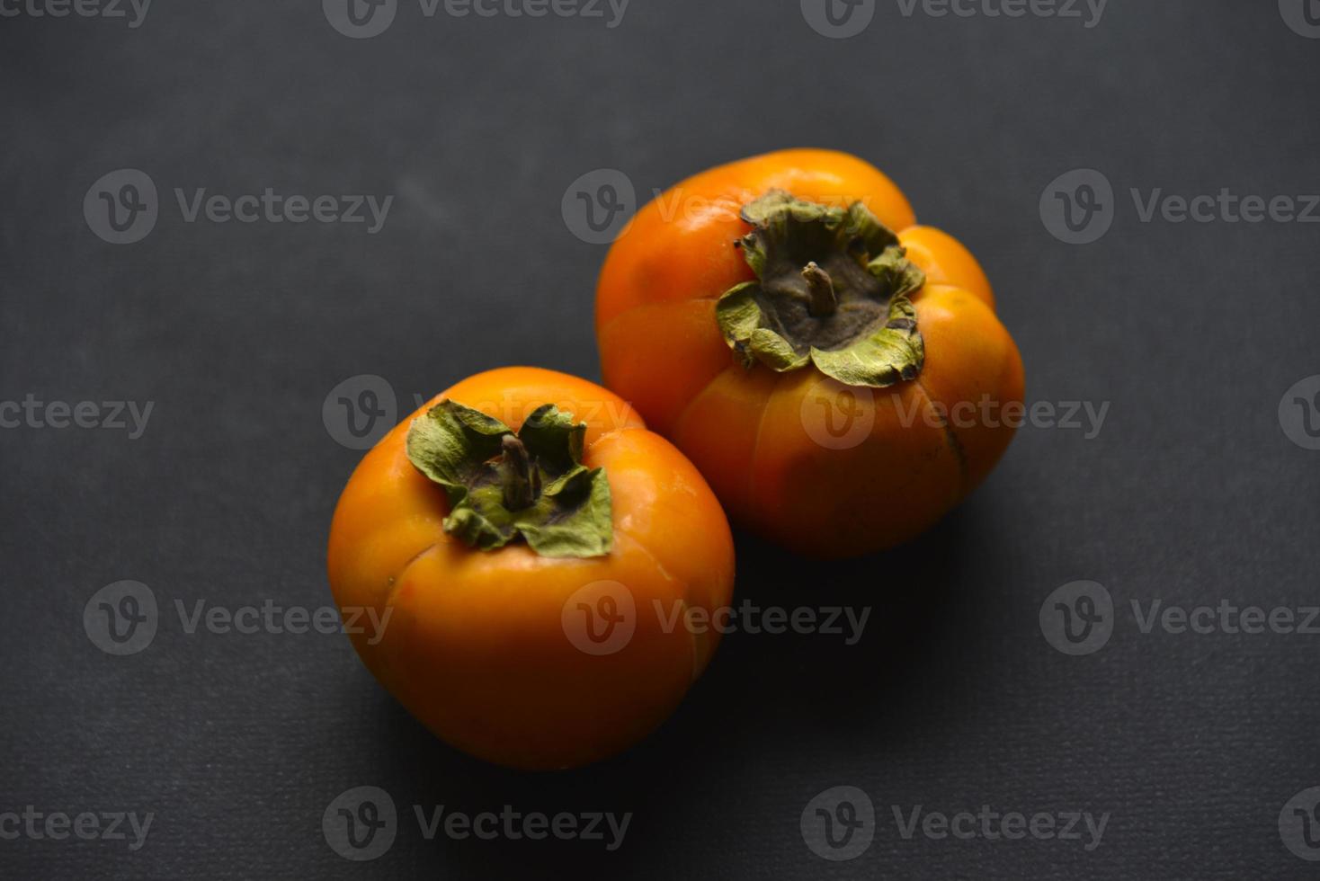 Orange persimmon fruits on a black background. Ripe and juicy persimmon fruits close-up. photo