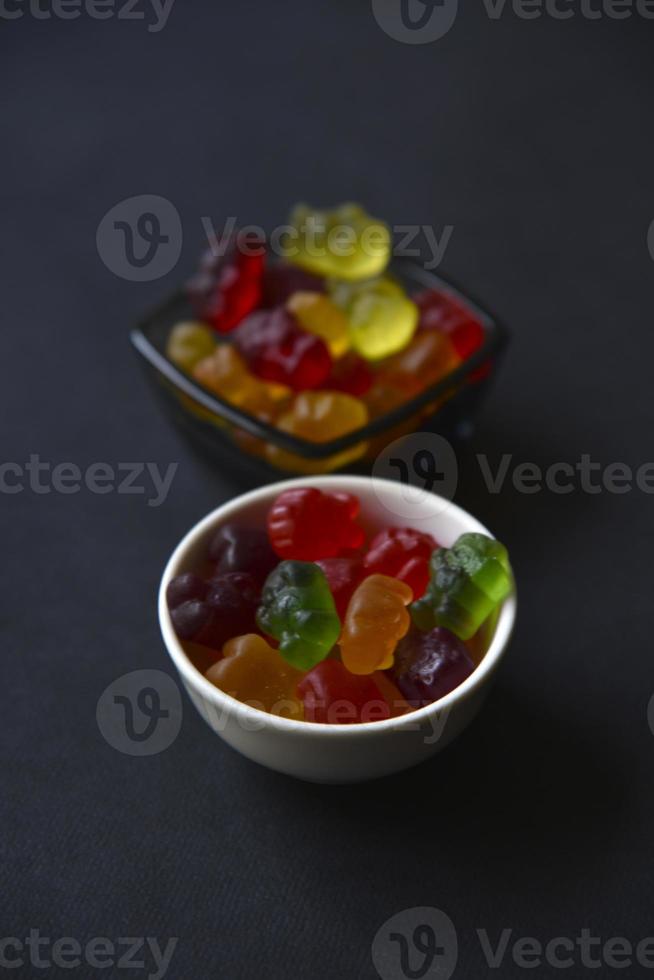 osos de mermelada de gelatina en una taza de cerámica sobre un fondo negro. primer plano de dulces coloridos de mermelada. textura de fondo foto
