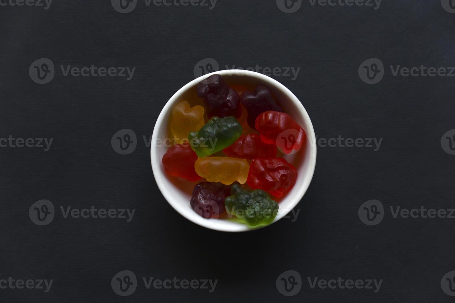 Jelly marmalade bears in a ceramic cup on a black background. Marmalade colorful candies close-up. photo