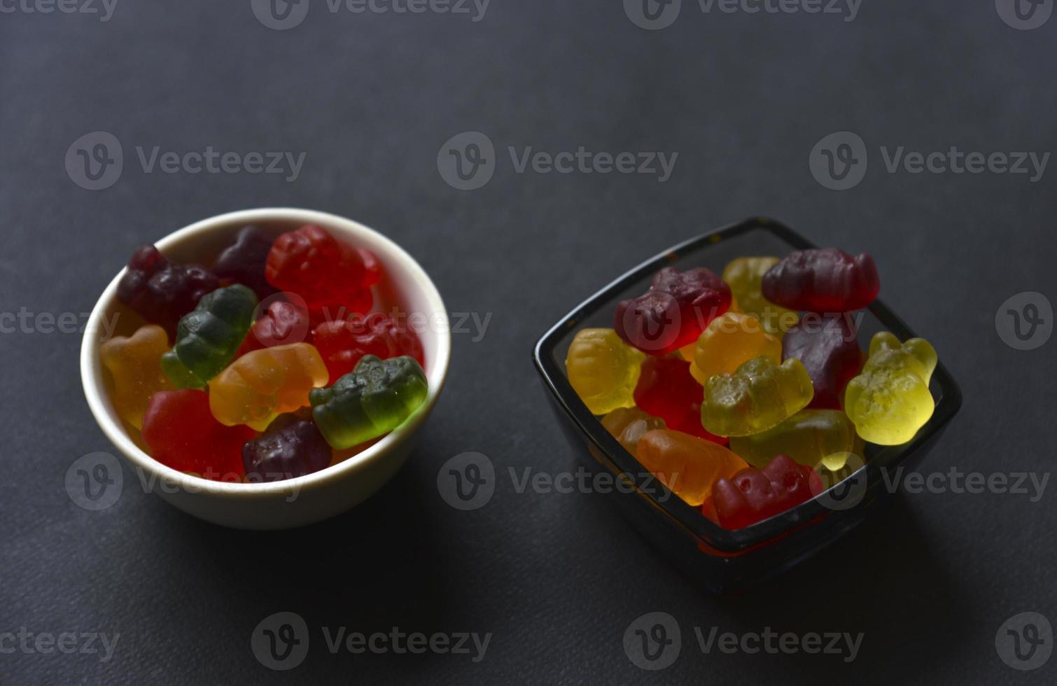 Jelly marmalade bears in a ceramic cup on a black background. Marmalade colorful candies close-up. photo