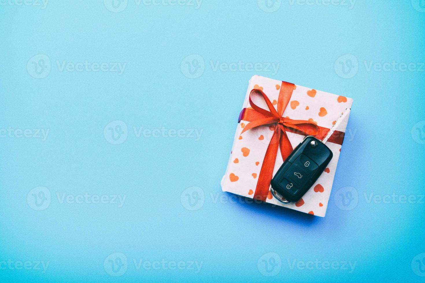Car key on paper gift box with red ribbon bow and heart on blue table background. Holidays present top view concept photo