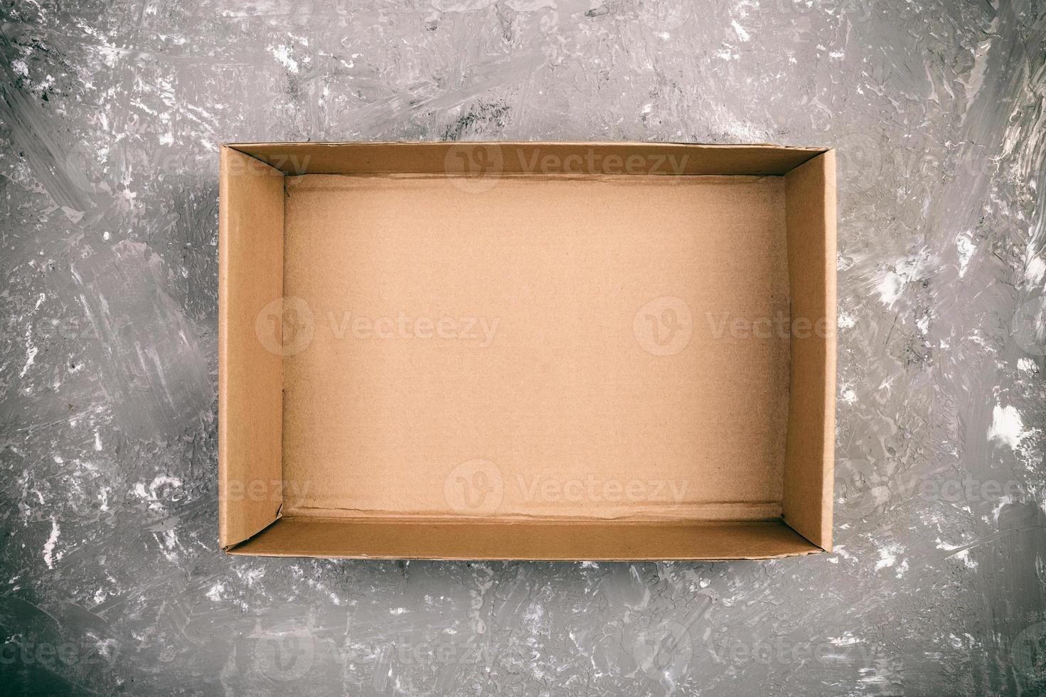 Opened brown blank cardboard box on cement gray background vintage, toned, top view photo
