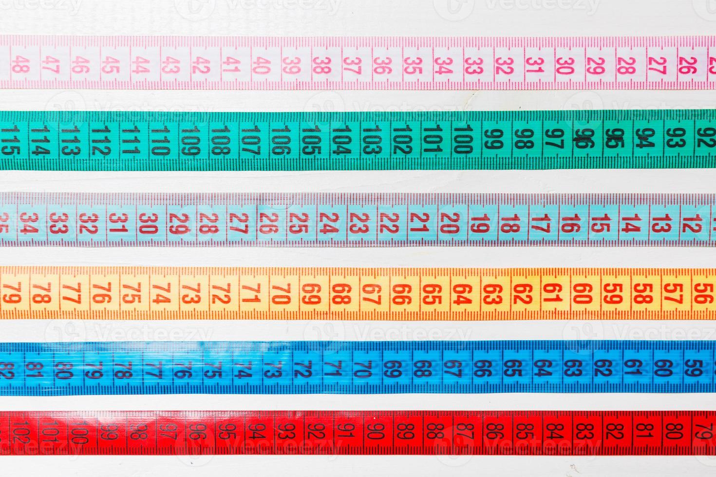 Close up of a group of colorful measure tapes lying in rows as a background. Diet concept on wooden background photo