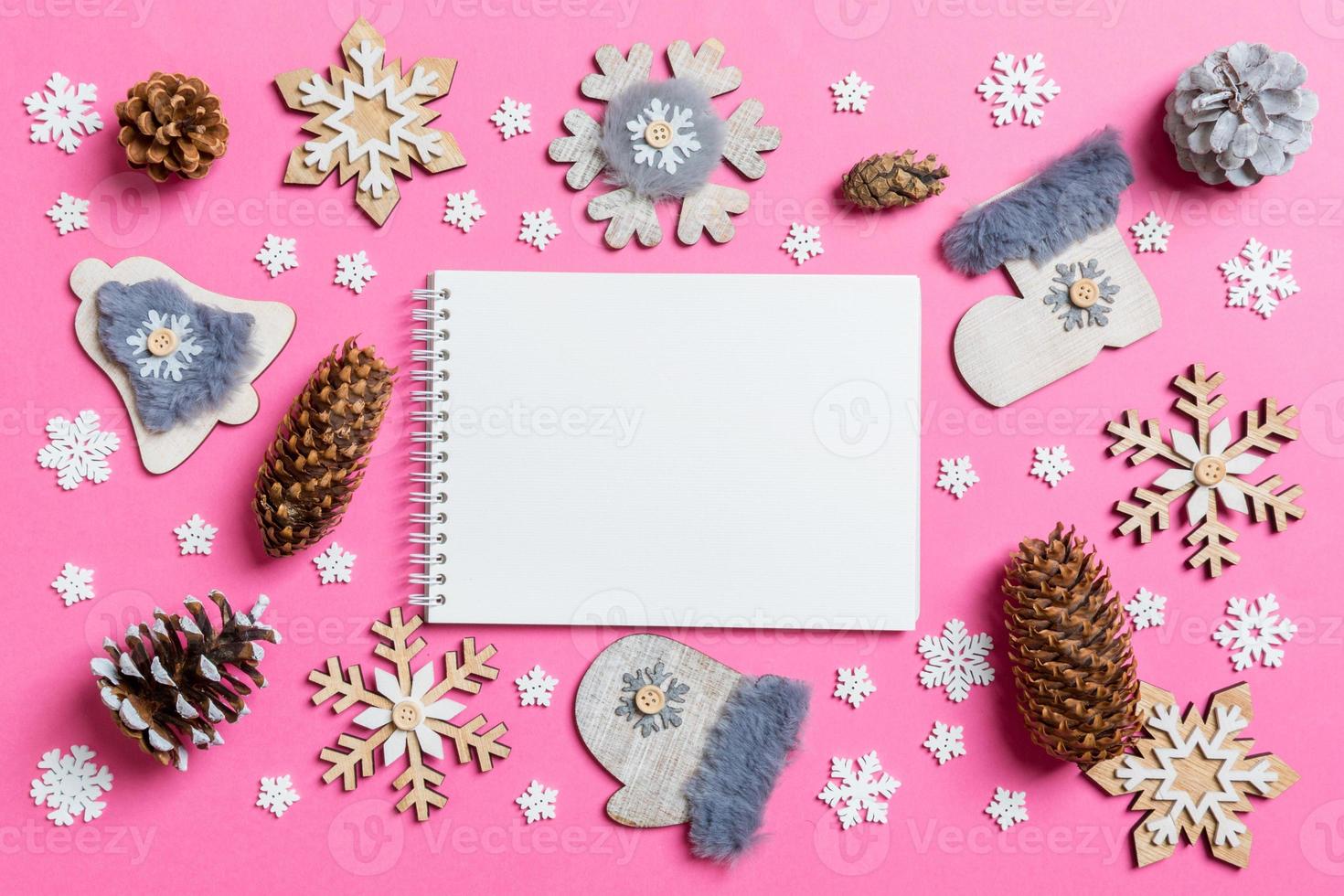Top view of notebook, holiday toys and decorations on pink Christmas background. New Year time concept photo