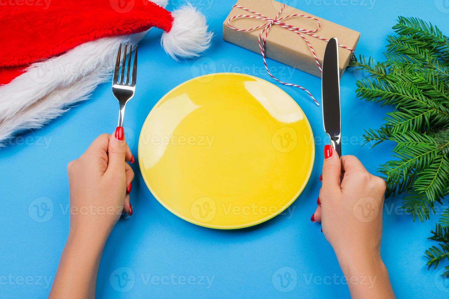 Hungry woman waiting for meal. empty yellow plate on a blue background with Christmas branches, santa hat and gift box. perspective view for your design photo