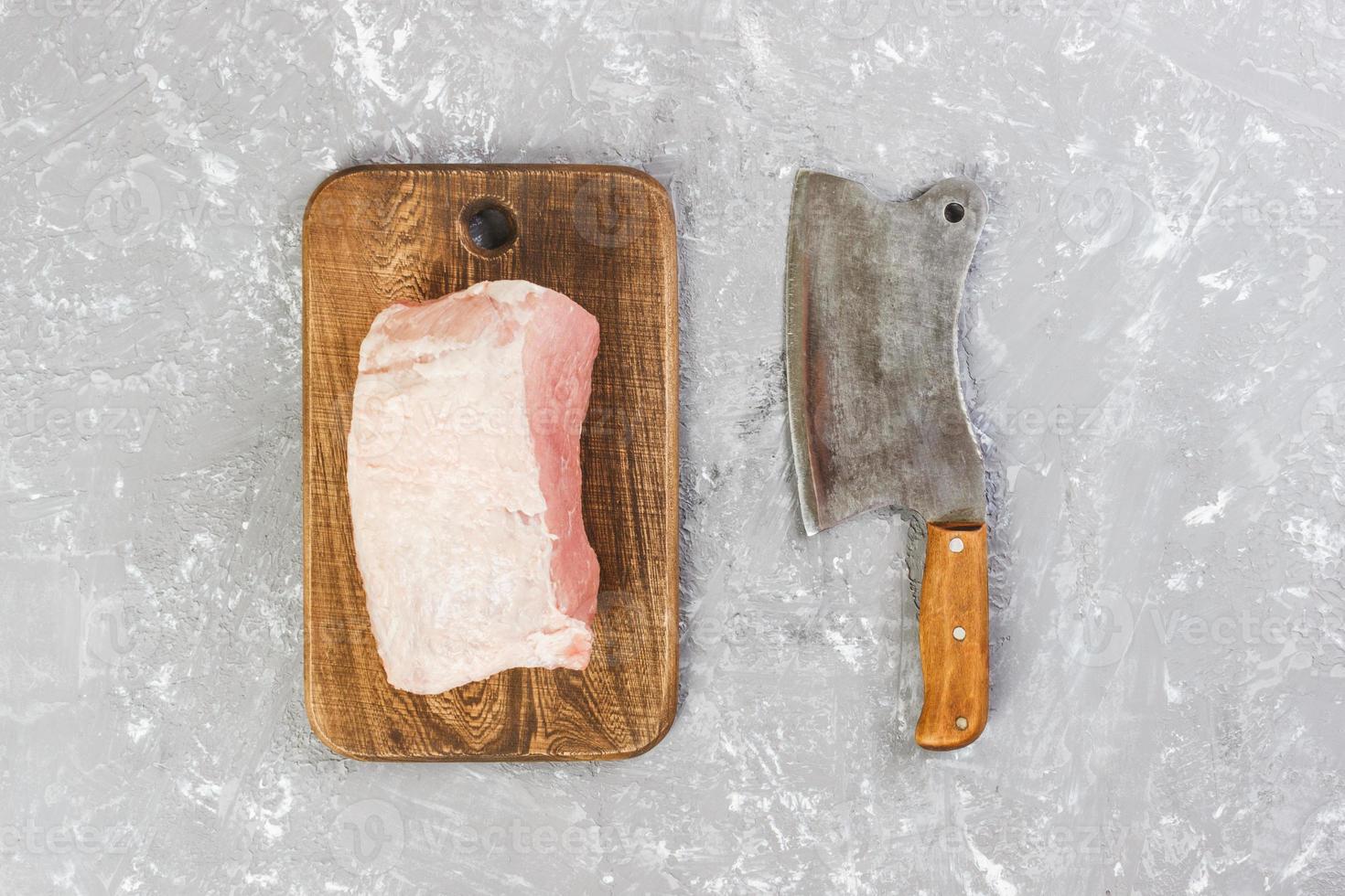 Raw cut of pork shoulder on board with knife or Kitchen ax. cleaver with fresh raw meat on gray concrete background photo