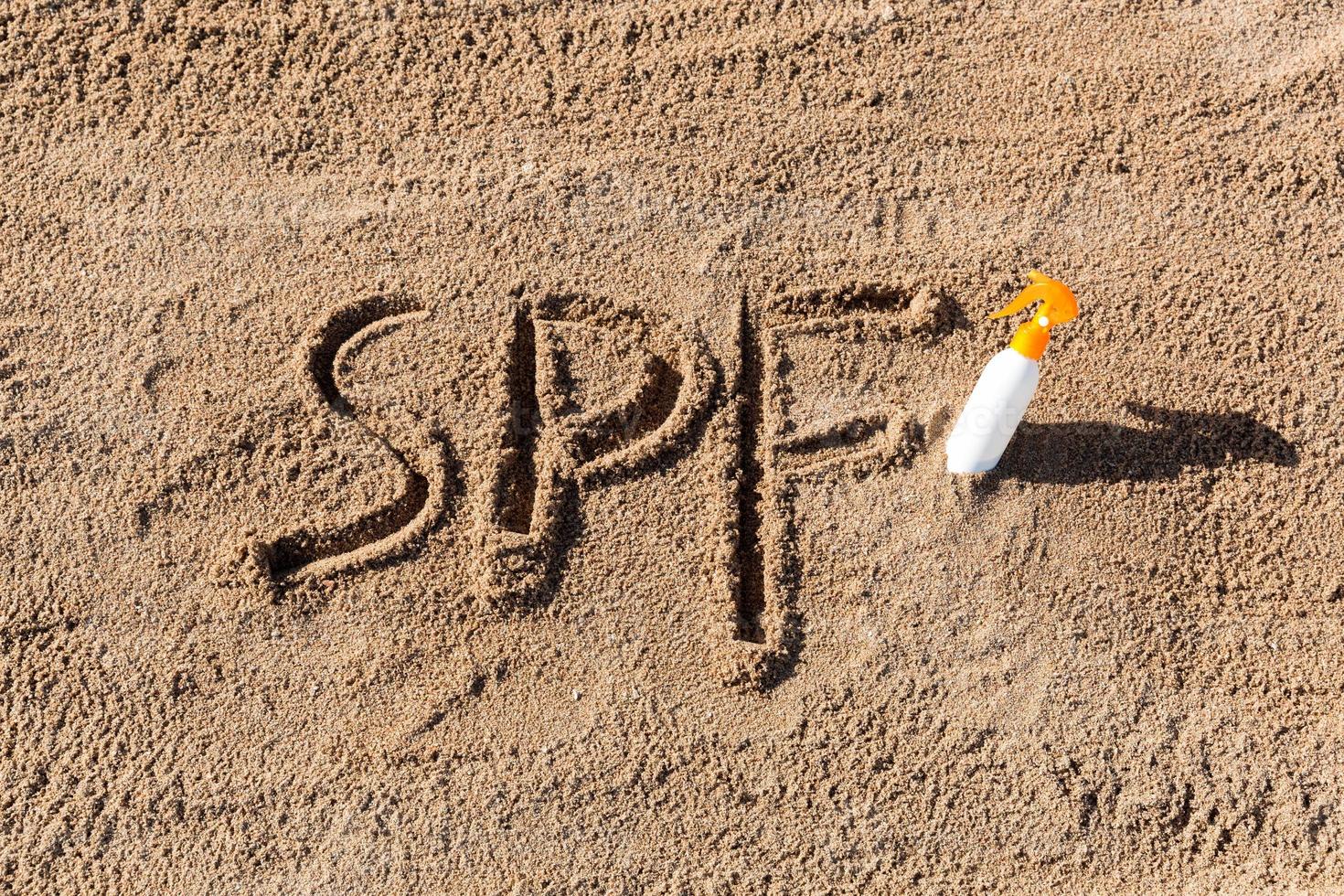 Sun protect factor. SPF word written on the sand and white bottle with suntan cream. Skin care concept background photo