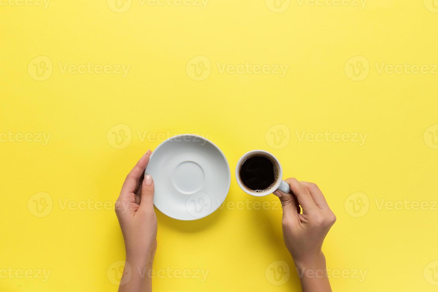 High angle of woman hands holding coffee cup on yellow background Minimalistic style. Flat lay, top view isolated photo